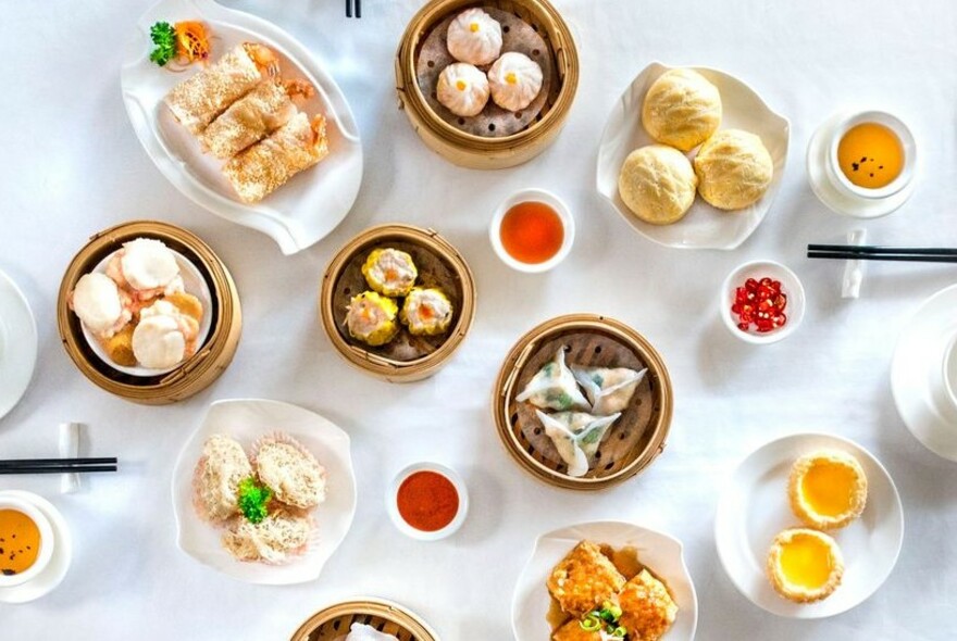 Assortment of dishes on a white table, including dumplings, buns and rolls.