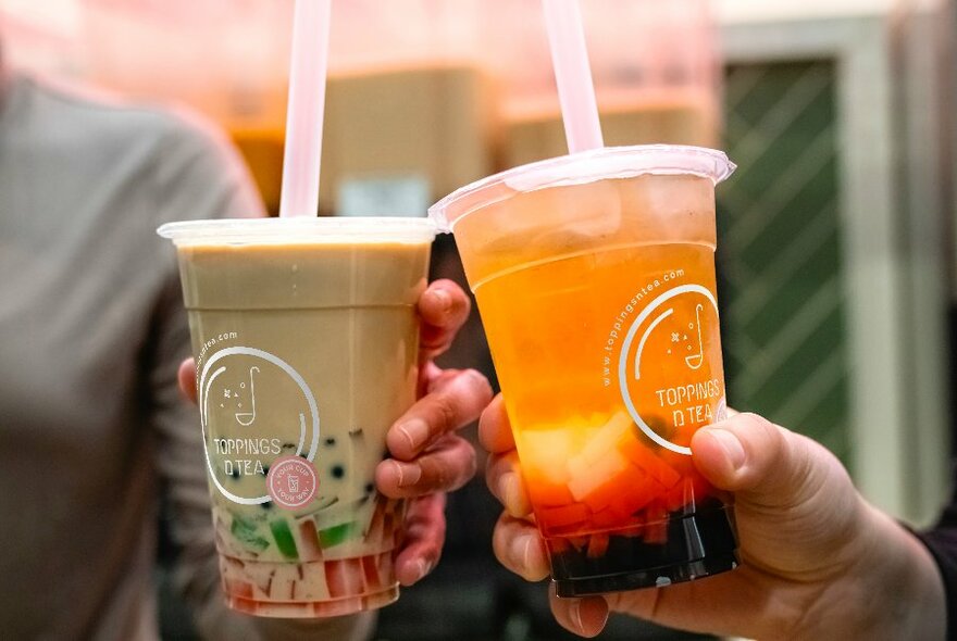 Two people clinking their colourful bubble tea drinks together. 