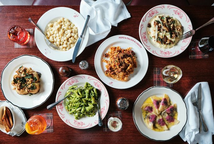 Overhead view of a table loaded with plates of pasta, salads and drinks.