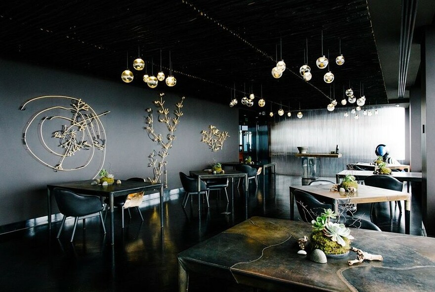 Moodily lit Vue de Monde interior with grey walls, plain chairs and tables with plant decor. 