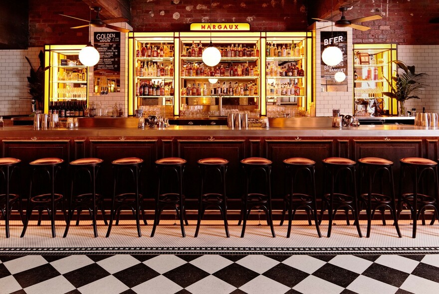 Bar stools lined up at a bar with black and white chequered floor pattern.