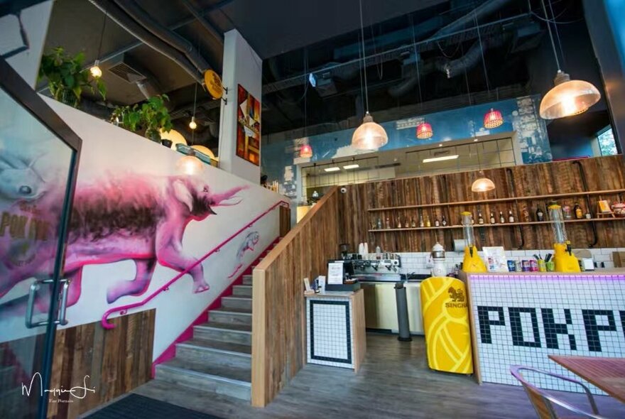 The interior of a restaurant showing stairs and a mural of a  pink elephant. 