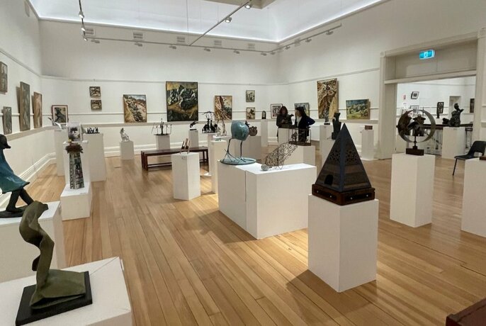 A gallery space with timber floors, white walls and many metal sculptures on white plinths.