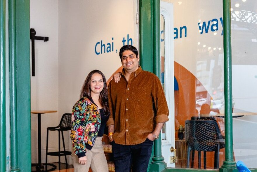 Two people, the owners of the Original Chai Co, standing on the footpath outside their shop.