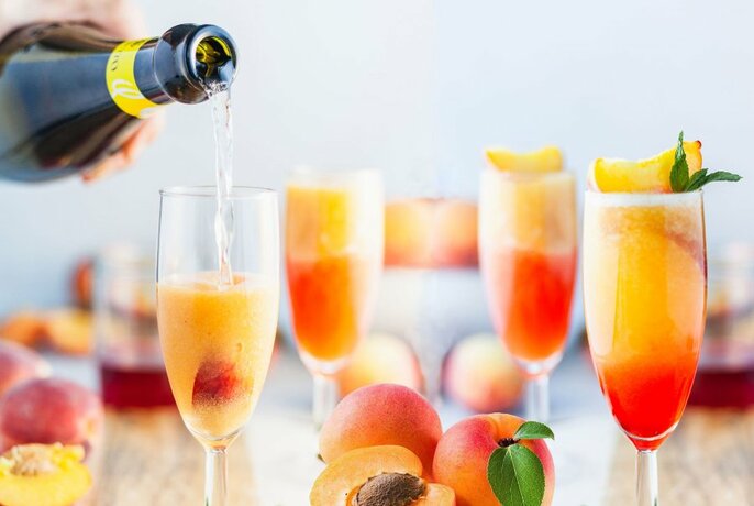 Champagne bottle being poured into flute with fruit, other glasses and apricots to right.
