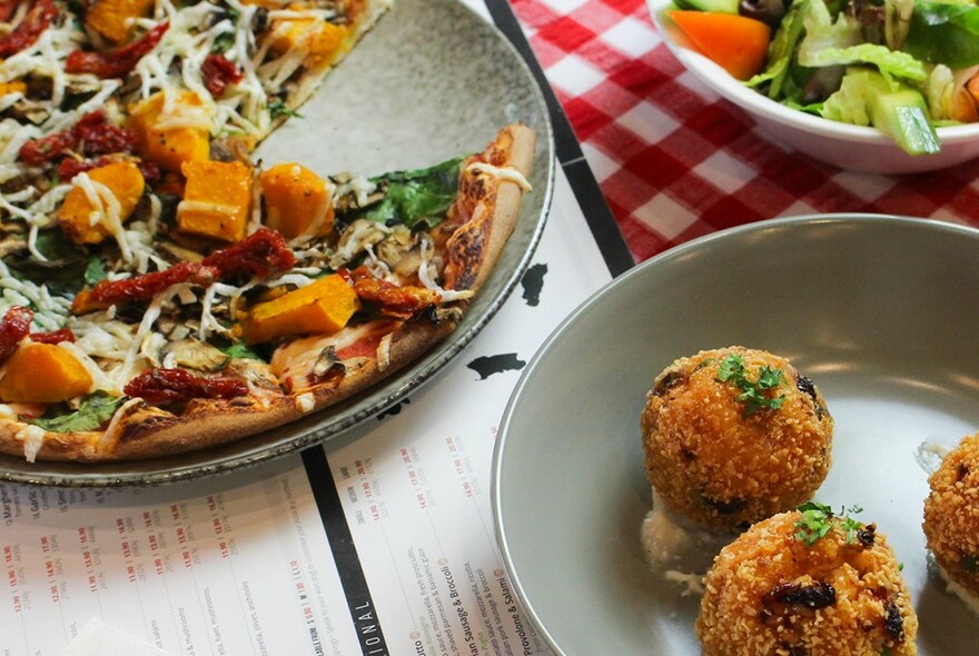 Pumpkin pizza and arancini balls on plates on a table.