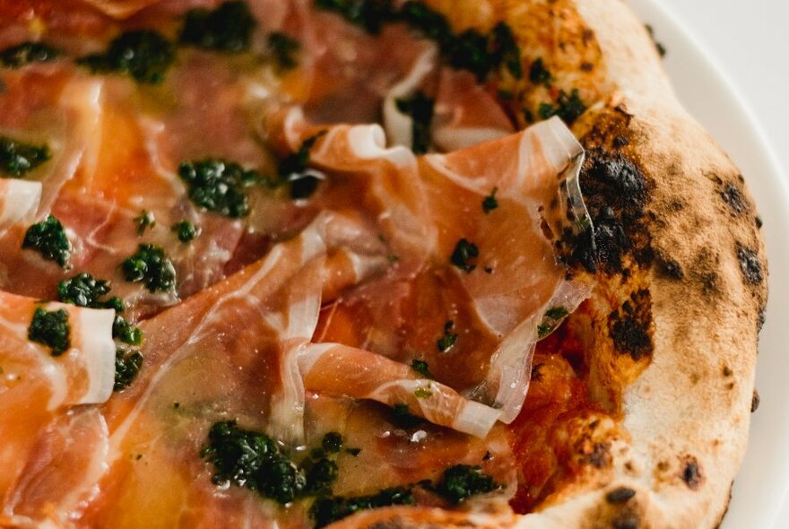 Detail of a pizza with ham and capers on a white plate.