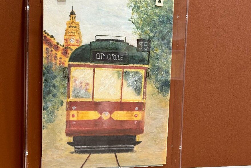 A painting of an old-fashioned W-class Melbourne tram, recreated in chocolate, displayed on a wall behind glass.