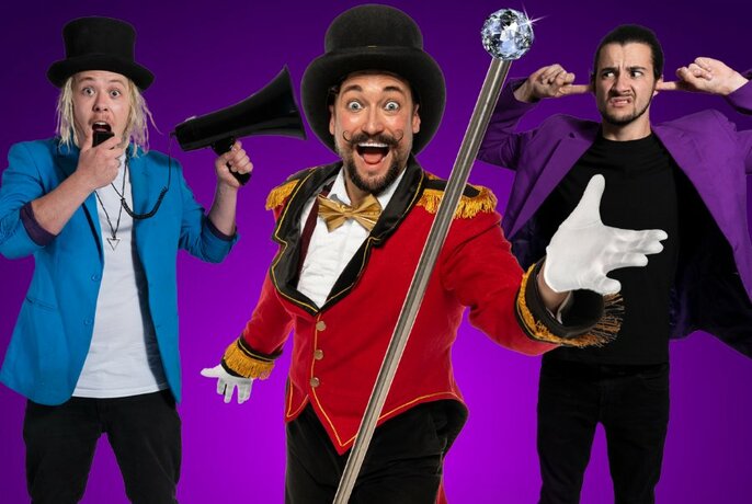 Three male performers wearing brightly coloured jackets posing against a purple background, one blowing a whistle, one with his fingers in his ears and one wearing white gloves and playing the part of the circus ringmaster.