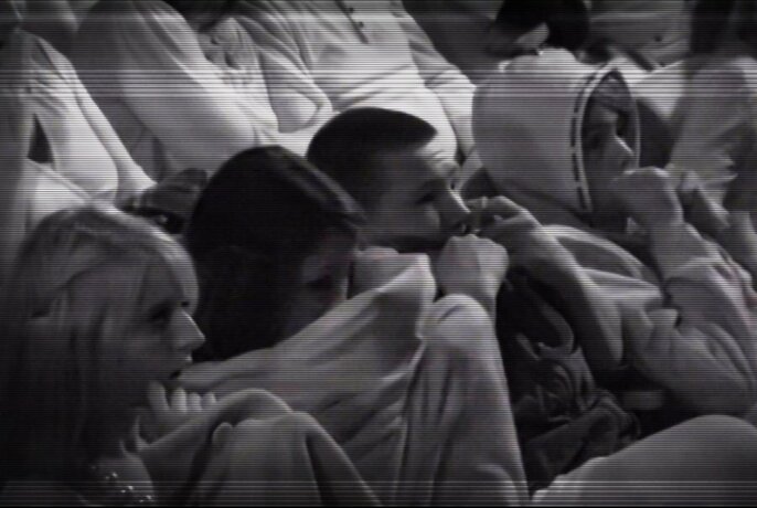 Black and white image of audience members watching something and looking scared and covering their eyes.