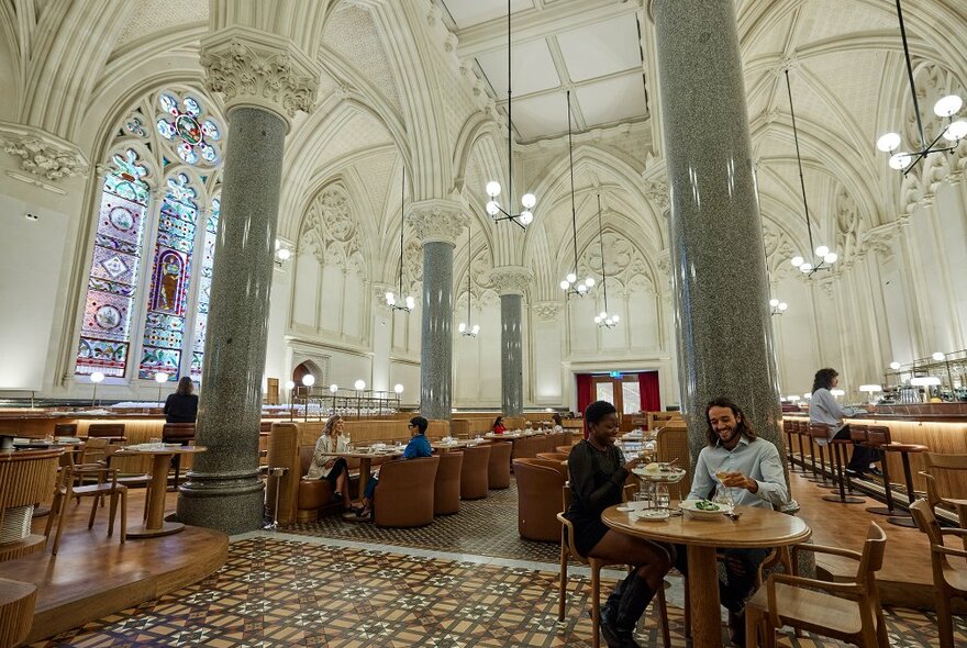 A couple sharing a meal in a large restaurant with high ceilings and stained glass windows.