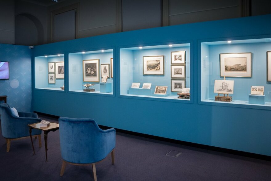 Blue illuminated display cases in an exhibition venue displaying artworks and documents.