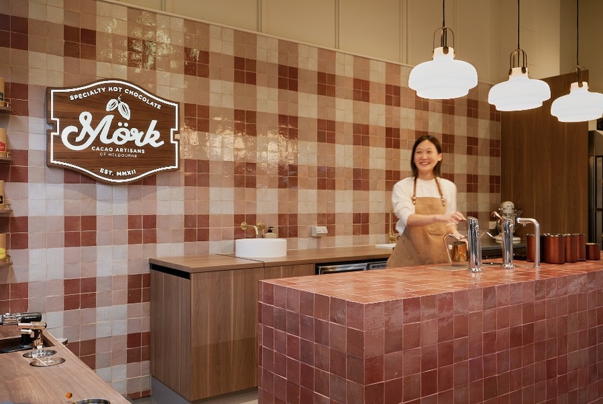 Shop interior with pink-tiled counter and woman standing and smiling behind.