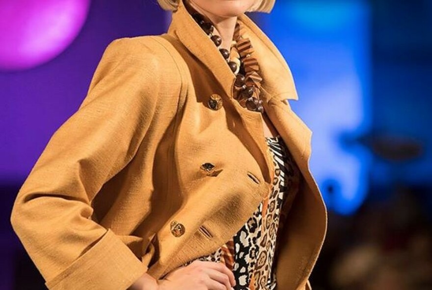 Model with hand on waist wearing a brown trench coat and animal print top.