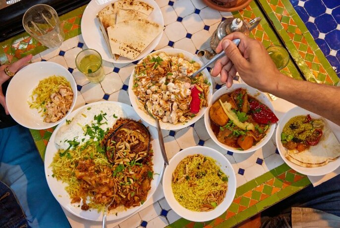 Overhead view of plates of food on a table, including rice, a vegetarian mixed plate, flat breads, and a hand holding a spoon to scoop up food.