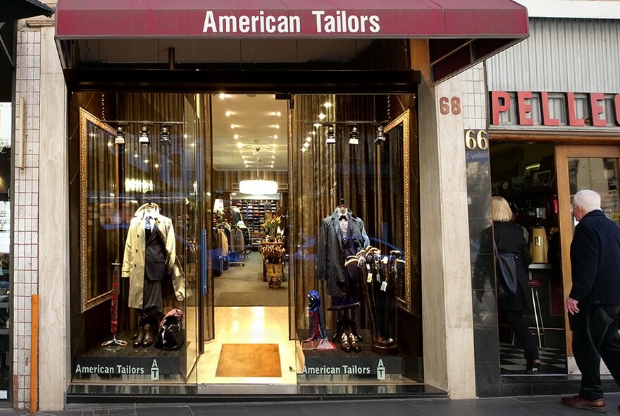 American Tailors exterior with window display of mannequins wearing suits, glimpse of Pellegrinis next door.