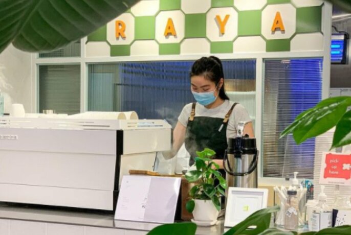 A barista wearing a mask and making coffee surrounded by greenery. 
