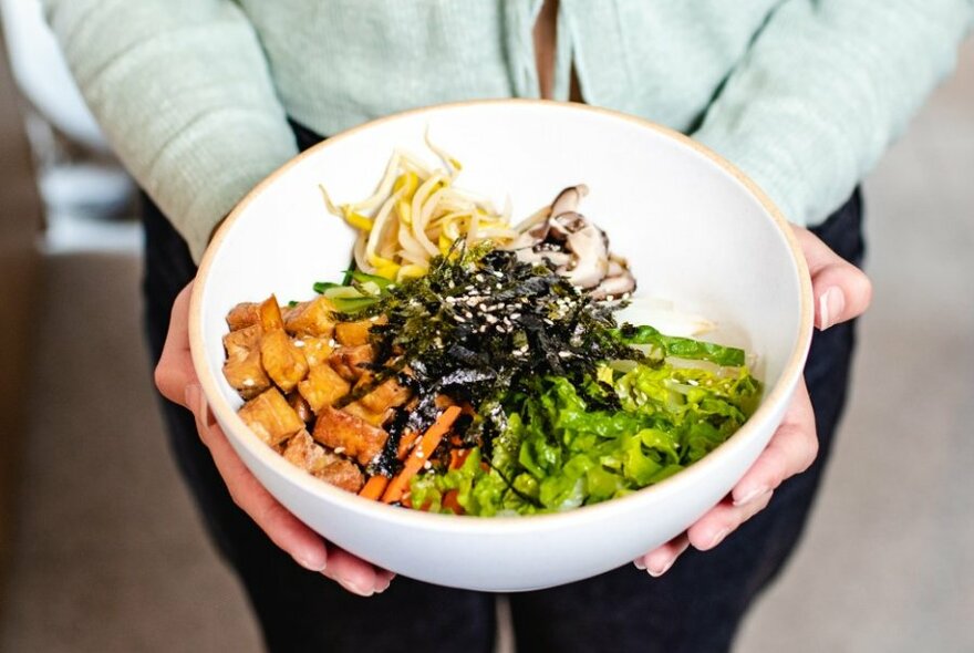 Someone holding a bowl of bibimbap with fresh vegetable toppings. 