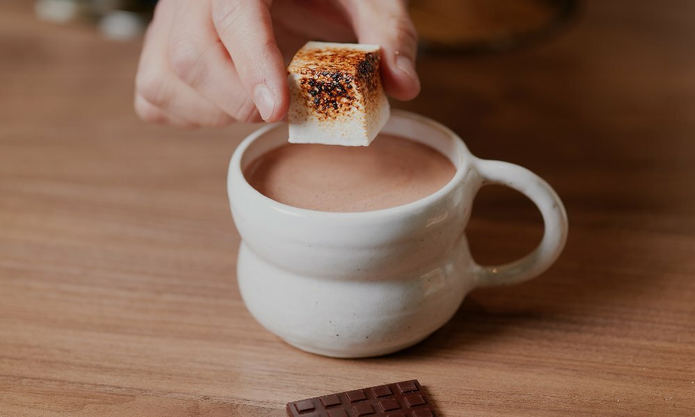 a person is putting a toasted marshmallow in a hot chocolate