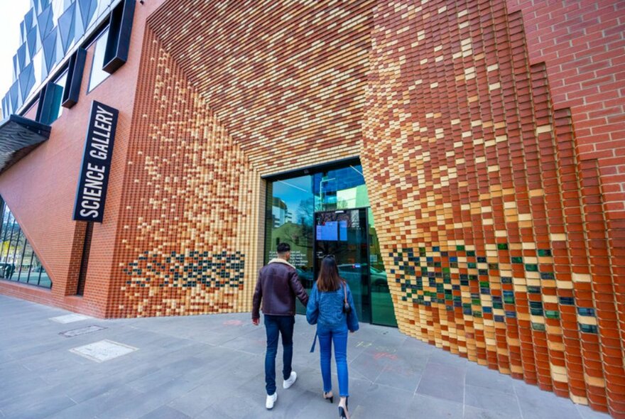 Two people walking into big brick building with 'Science Gallery' sign outside.