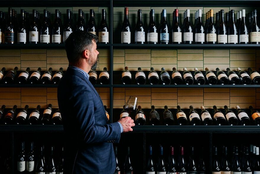 A man surveys a wall full of wine bottles.