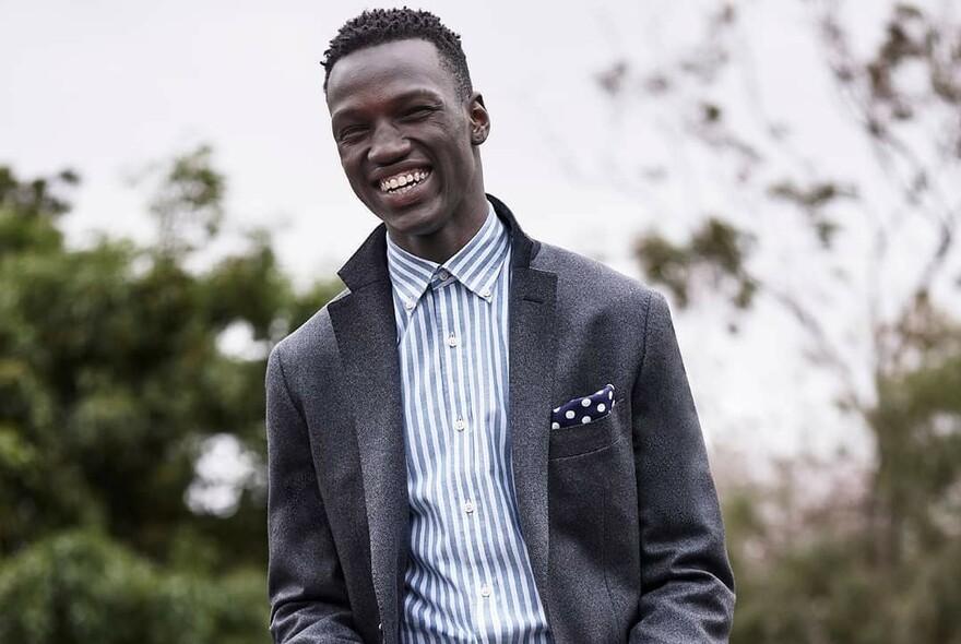 Smiling model wearing a striped shirt and grey jacket with the collar turned up.