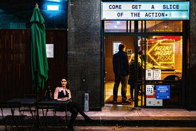 Woman sitting outside a pizza joint at night.