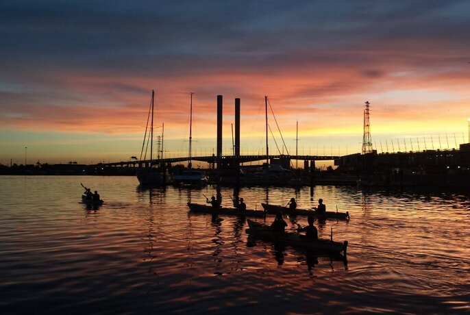 A sunset view of kayaks on the water, looking towards Bolte Bridge in Melbourne.