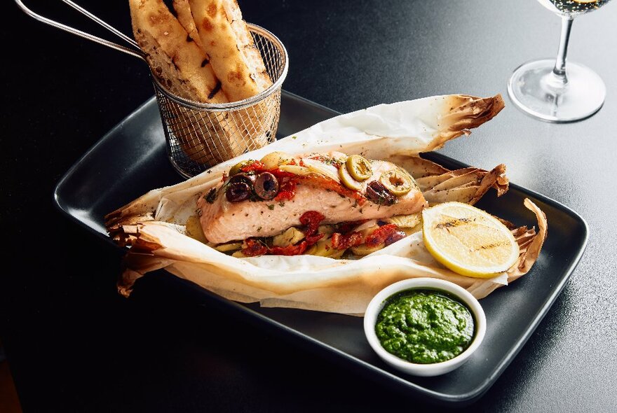 A platter of fish and vegetables served with a dish of green sauce and lemon.
