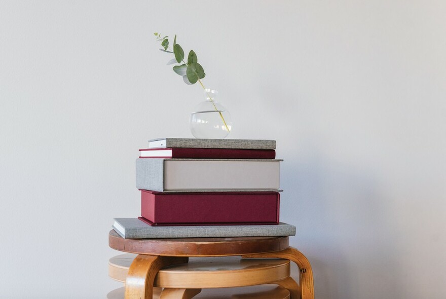Stack of red and grey notebooks on stacked wooden stools, with small vase and greenery atop.