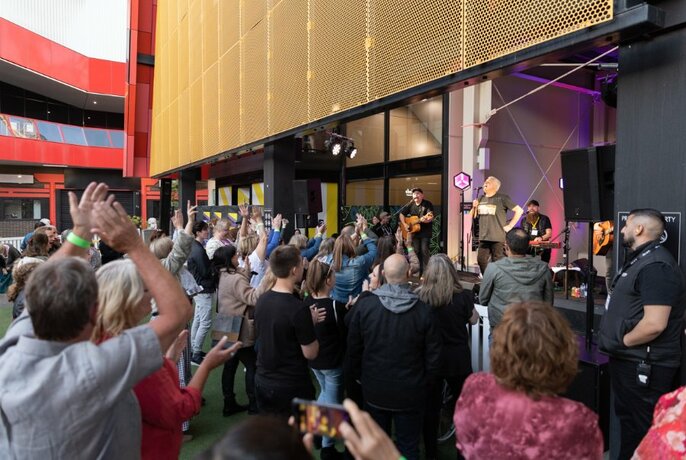 A crowd of people at The District Docklands cheering on performing musicians.