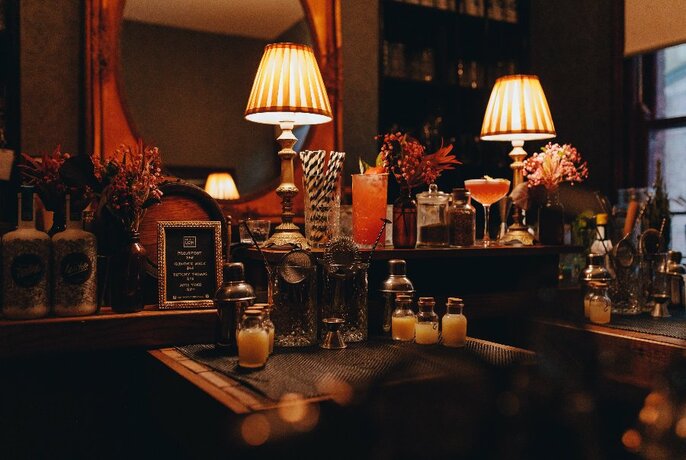 Close up of bar at Little Lon Distilling, with cocktail implements on a table and a large bronze-framed mirror and lamps behind.