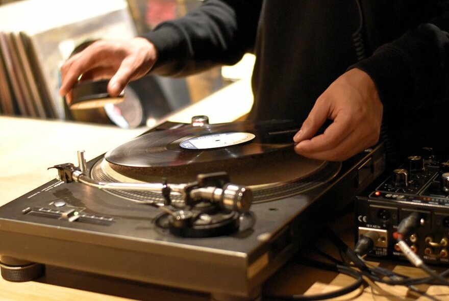 A pair of hands placing a vinyl record on a turntable.