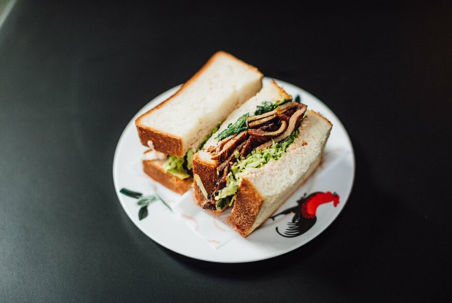 A sandwich of shokupan bread and meat and alfalfa filling on a patterned plate.