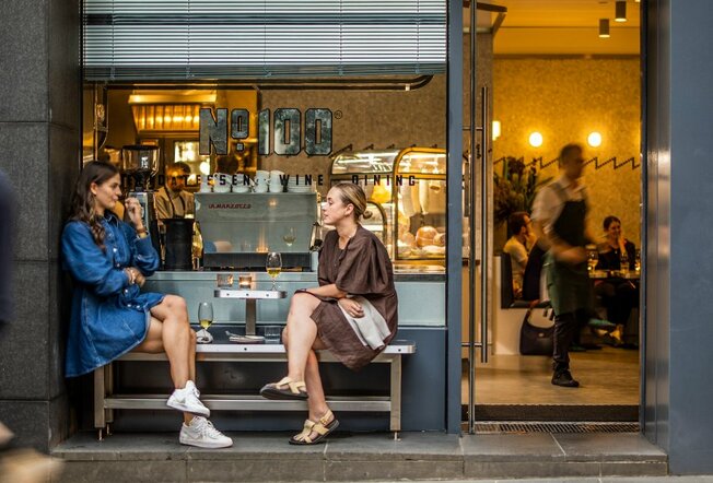 Two women sitting on a bench outside a cosy bar.