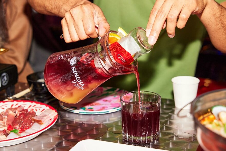 Someone pouring a red cocktail from a jug.