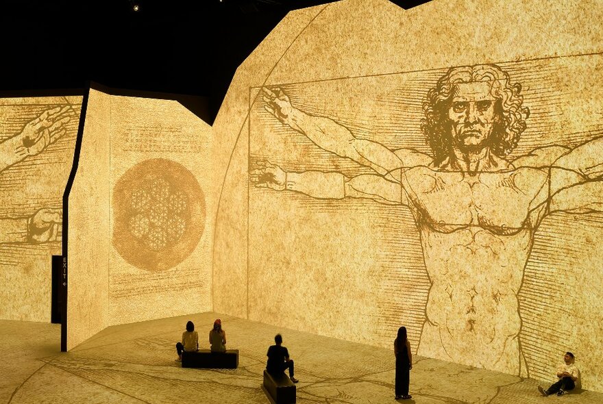 Inside a large digital gallery with a projection of Leonardo da Vinci's Vitruvian Man
