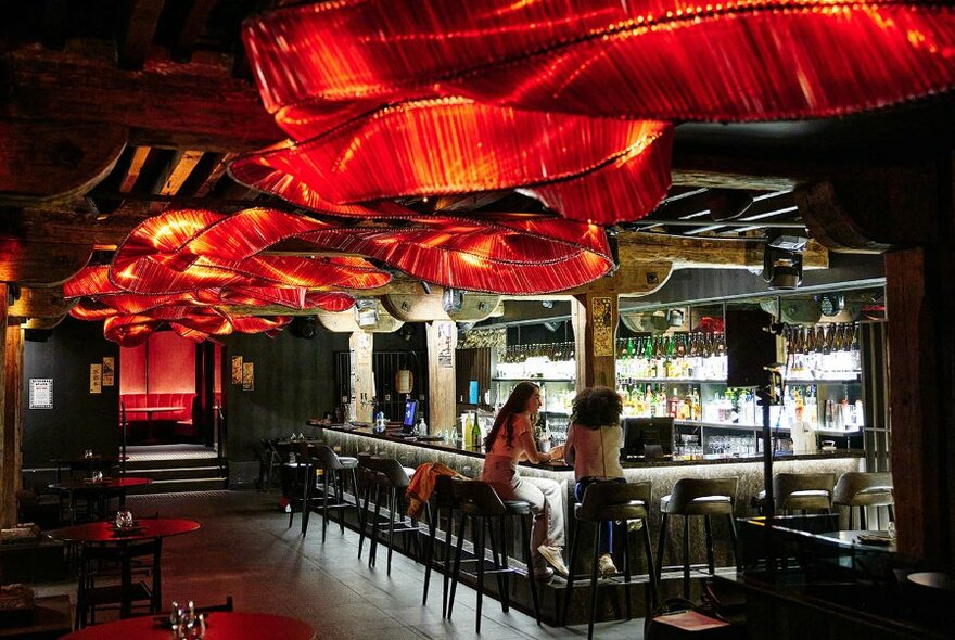 Two women dining at a bar with a red ribbon light sculpture on the ceiling.
