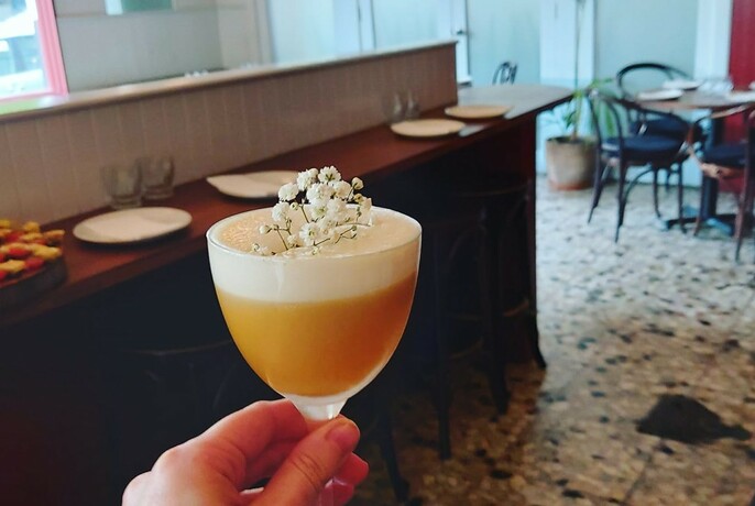 A foamy cocktail with floral garnish inside Bar Ampere.