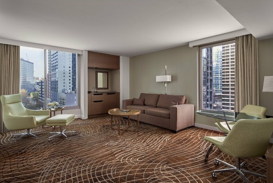 Corner suite at the Melbourne Marriott Hotel with  several green armchairs and a couch near large windows.
