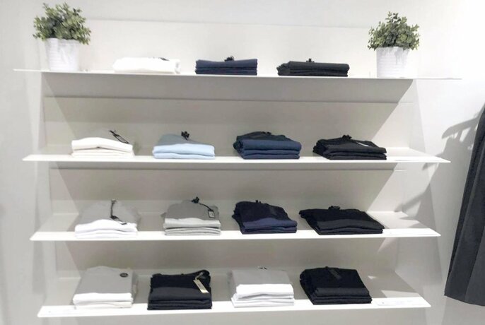 White shelves with neatly folded black, white and blue T-shirts.