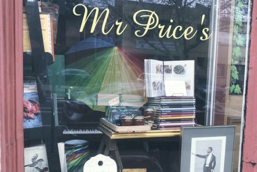The front window of Mr Price's Food Store showing books, a vintage picture and a rainbow-coloured umbrella.
