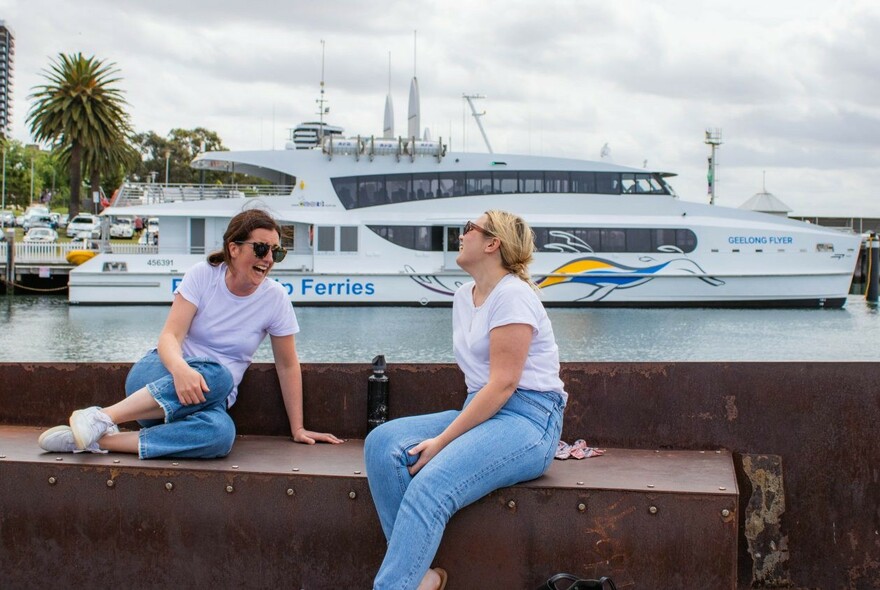 Two women laughing and seated in front of a ferry.