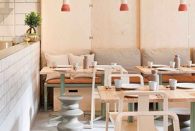White restaurant interior with blonde wood tables and chairs, white tiles and pendant lighting.