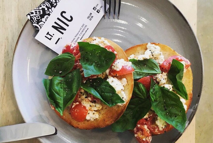 Bagels on a plate topped with tomato, basil and feta.