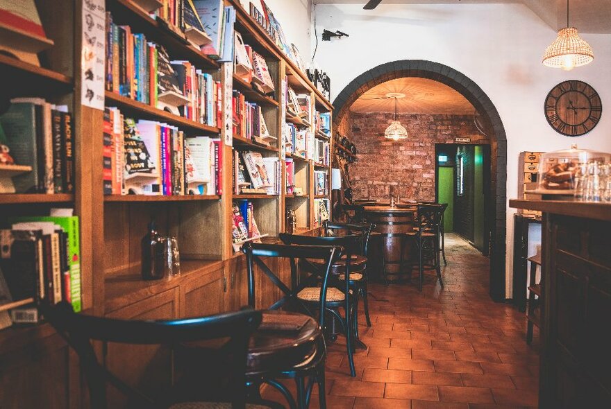 Cafe interior with bookcases lining the wall, wicker chairs and tables and view towards the back of the space.
