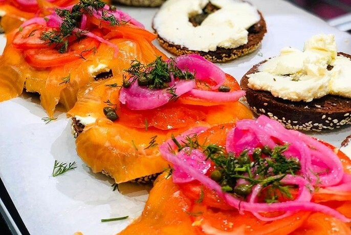 A platter of bagels topped with bright orange salmon and pickled onion, cream cheese spread on one half.