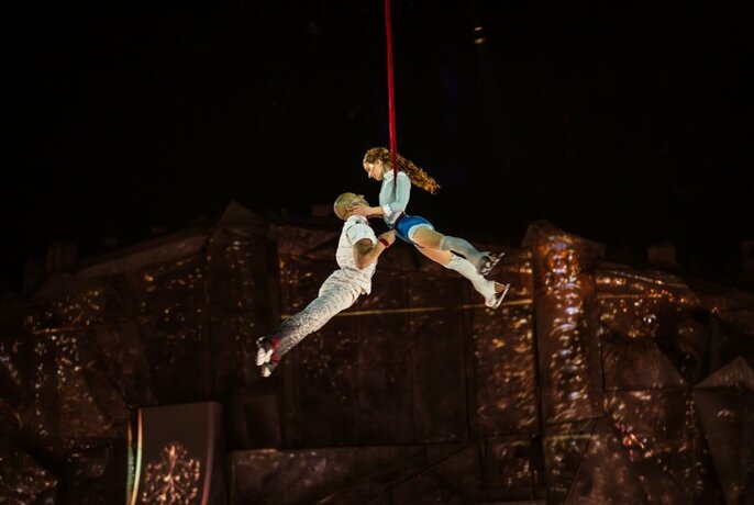 Two acrobats in mid-air held by a red rope. 