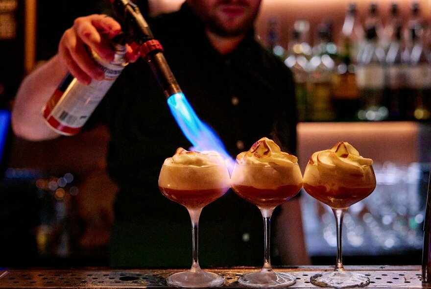 A bar tender is using a blow torch to make a cocktail