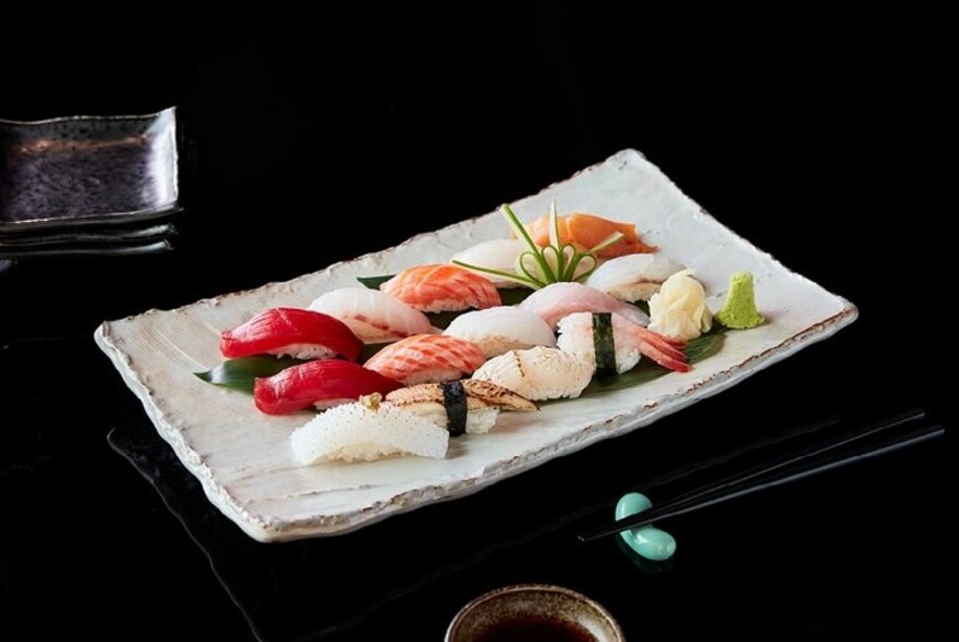 A white plate of mixed nigiri on a dark table.